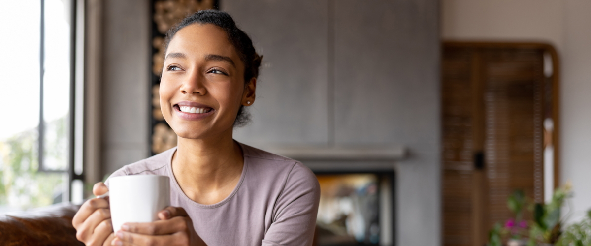 Happy African American woman drinking a cup of coffee at home and smiling